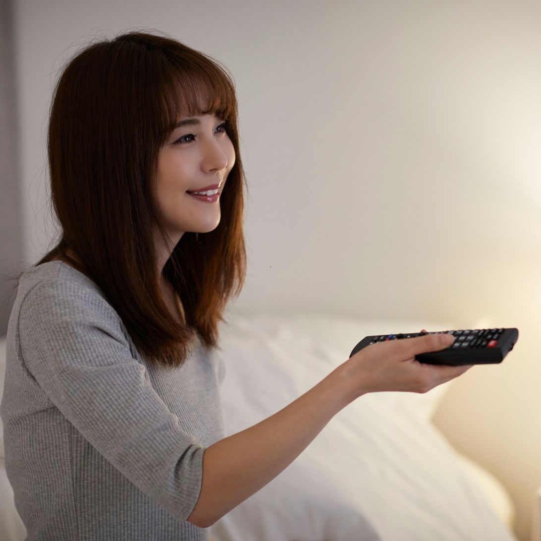 Vrouw zit op boxspring en gebruikt afstandsbediening voor tv-lift
