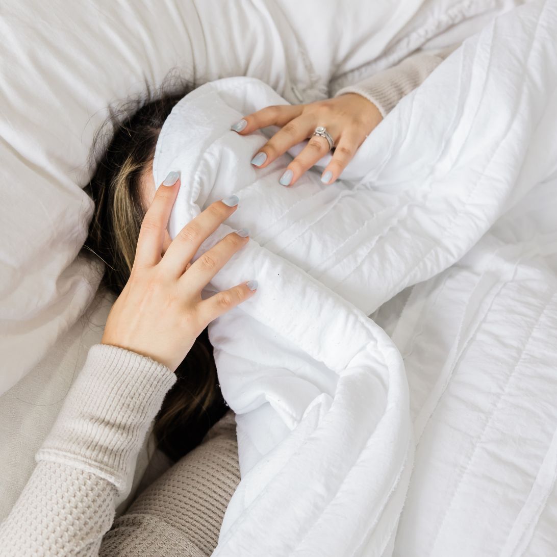Vrouw ligt in bed, onder deken, met Oura Ring aan
